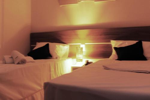 two beds in a hotel room with white sheets at Assay Plaza Hotel in Hortolândia