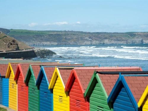 a row of colorful beach huts next to the ocean at The Old Auction Rooms Lot 2 Central with Private Parking in Whitby