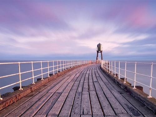 a wooden pier with a lighthouse in the water at The Old Auction Rooms Lot 2 Central with Private Parking in Whitby