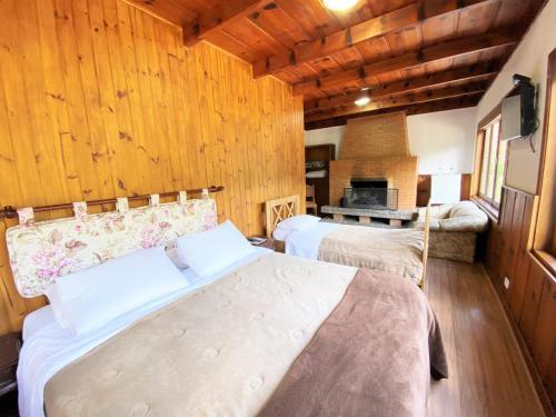 two beds in a room with wooden walls and wooden floors at Pousada do Sino - 2 min do Capivari in Campos do Jordão