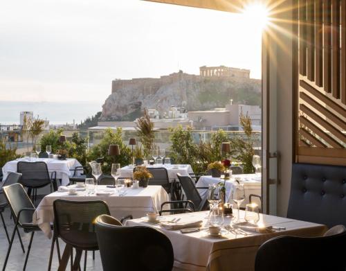 a restaurant with tables and chairs with a view of the acropolis at Electra Hotel Athens in Athens
