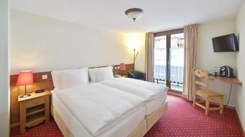 a hotel room with a large white bed and a window at Le Chamois in Les Diablerets