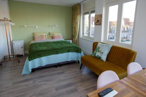 a bedroom with a bed and a couch and windows at El Puerto Bed and Breakfast in Hoorn