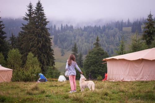 a girl with a dog in a field with tents at Eco glamping - Carpathians. Retreat hub Dzin Space in Verkhovyna