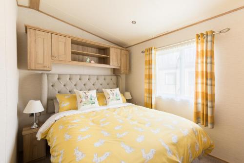 a bedroom with a bed with a yellow comforter and a window at Cottontail Lodge - Hot tub - Pet Friendly in South Cerney