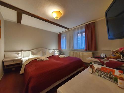 Habitación de hotel con cama roja y TV. en Hotel Zur Goldenen Sonne en Quedlinburg