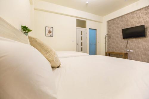 a white bed with pillows and a television on a wall at Square B&B in Taitung City