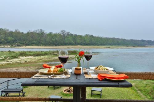 a table with two glasses of wine and food on it at Jungle Villa Resort - Near Chitwan National Park in Chitwan