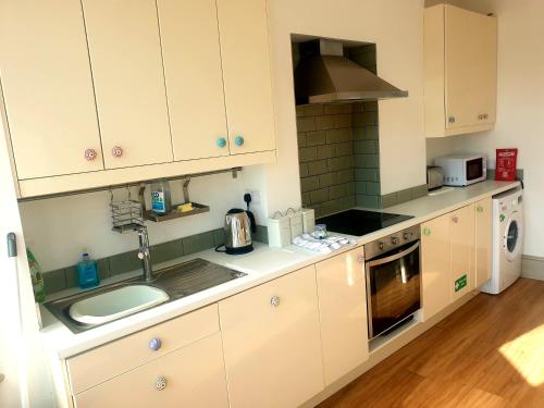 kuchnia z białymi szafkami, zlewem i kuchenką w obiekcie Upper Rooms Seaford w mieście Seaford