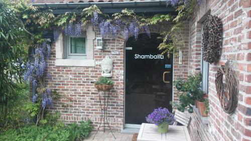 a brick building with a door with purple flowers at SHAMBALLA logies nieuw en zeer verzorgd appartement met voortuin en terras in Deinze
