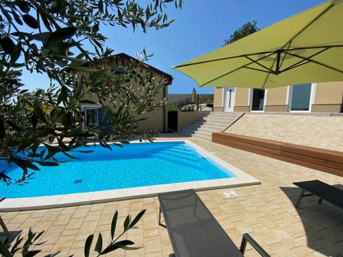 a swimming pool with an umbrella next to a house at Vila Porto Olive Heated Pool near Piran & Portorož in Portorož