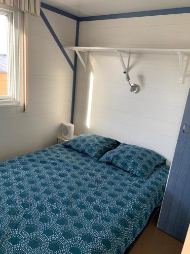 1 dormitorio con cama con sábanas azules y ventana en Mobil home climatisé ETANG DE BESSE, en La Parée Preneau