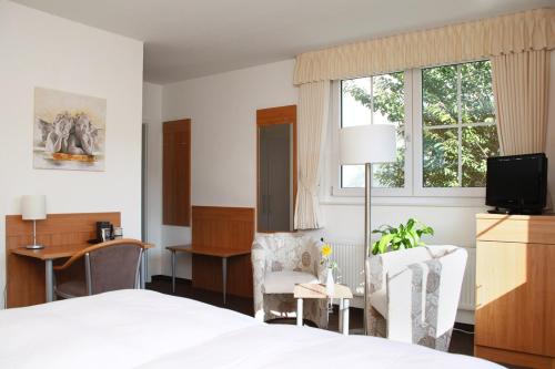 a bedroom with a bed and two chairs and a tv at Hotel Fürstenberg in Essen