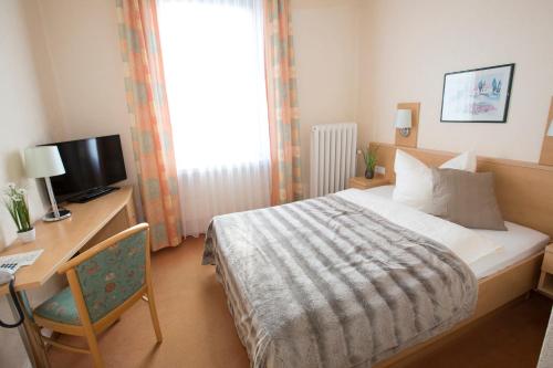 a bedroom with a bed and a desk and a television at Hotel-Restaurant Wilhelmsbad in Seesen