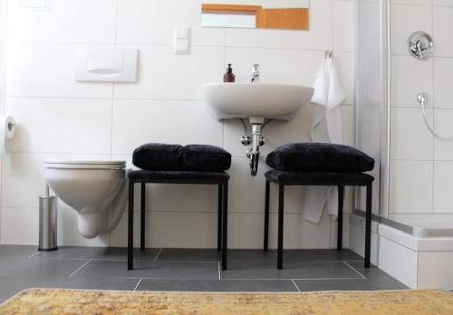 a bathroom with a sink and a toilet and two stools at Piesteritzer Hof - Hotel Garni in Lutherstadt Wittenberg