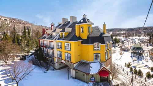 une grande maison jaune avec de la neige au sol dans l'établissement La Tour des Voyageurs II, à Mont-Tremblant