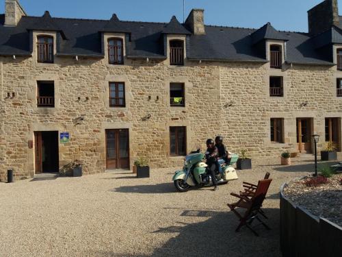 two people riding a scooter in front of a building at Chambres d'Hôtes La Rompardais in Pléven
