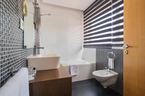 a bathroom with a sink and a toilet and a tub at Hotel Farol in Praia da Barra