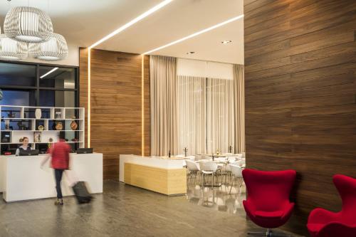a lobby with red chairs and a person standing in front of a counter at Fiesta Inn Chihuahua Fashion Mall in Chihuahua