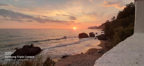 a sunset on a beach with the ocean and rocks at Kostas Beach Apartments in Agios Gordios
