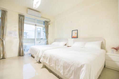 two beds in a white room with a window at Square B&B in Taitung City