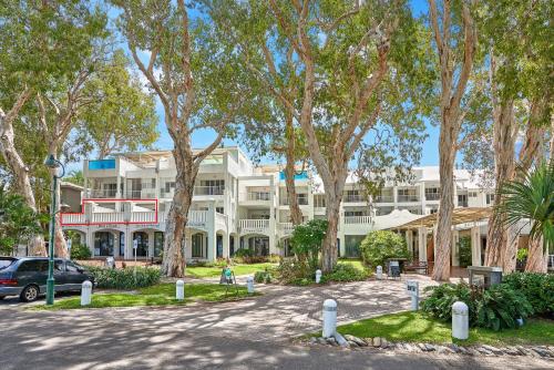 a large white building with trees in front of it at Beach Club Private Apartments Palm Cove in Palm Cove