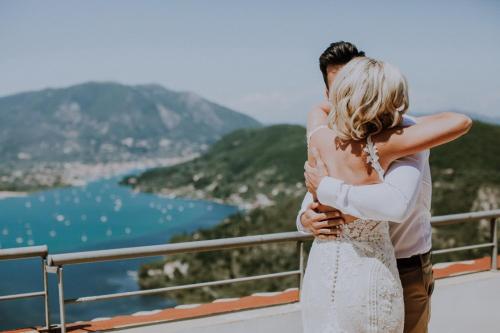 a bride and groom hugging on a balcony overlooking the water at marmar villas in Vlikhon