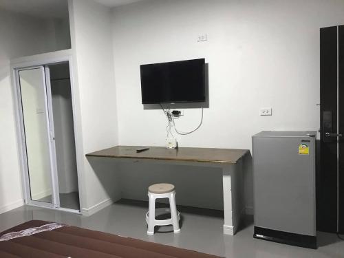 a desk with a television on a wall next to a refrigerator at ไนท์ ฟอร์ ยู เรสซิเดนซ์ in Buriram