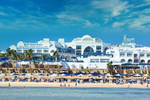ein Strand mit Sonnenschirmen und ein großes weißes Gebäude in der Unterkunft Pickalbatros Palace Sharm - "Aqua Park" in Sharm El Sheikh