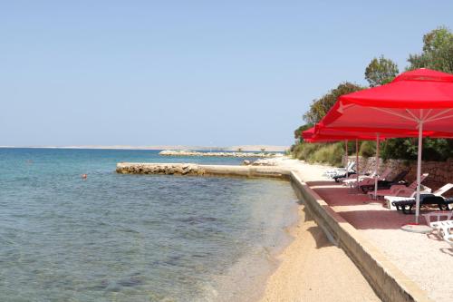 a beach with chairs and red umbrellas and the water at Vila Stosic in Ražanac