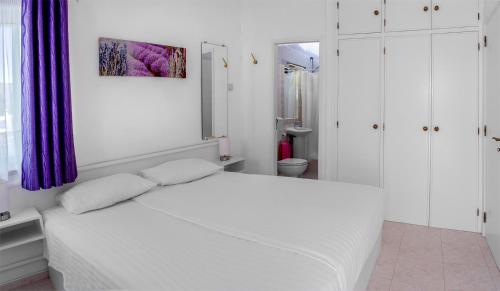 ein weißes Schlafzimmer mit einem weißen Bett und einem violetten Vorhang in der Unterkunft Stylish two bedroom apartment with garden vieuw in Luz