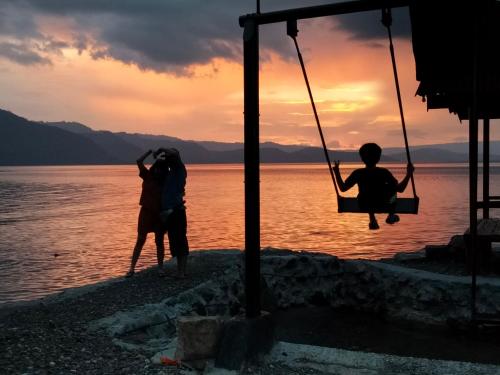 two people sitting in a swing on the beach at sunset at Pondok Berata Dapdap in Balige