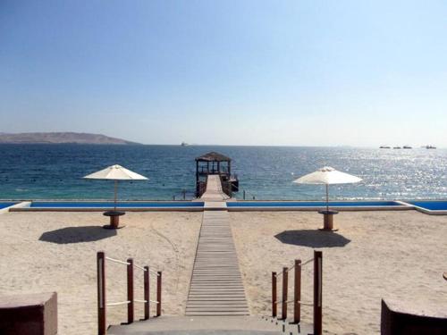 a dock with umbrellas on a beach next to the ocean at Paracas top tower beach front in Paracas