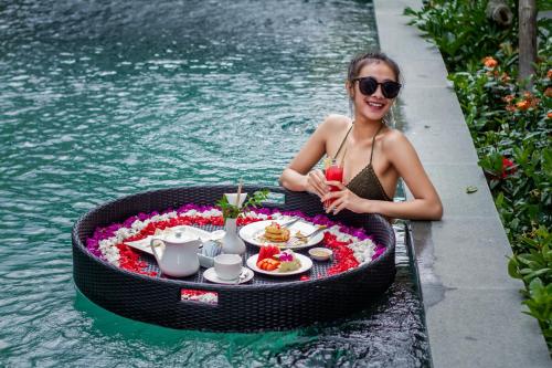 una mujer sentada en una mesa circular con comida en el agua en Tri Dewi Residence by Pramana Villas en Ubud