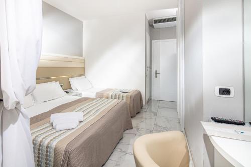 a small room with two beds and a chair at Hotel Mediterraneo in Lignano Sabbiadoro