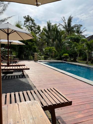 a swimming pool with benches and an umbrella next to it at Red island villas in Banyuwangi