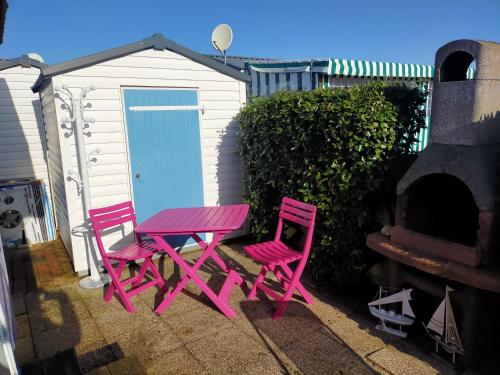 dos sillas rosas y una mesa de picnic al lado de un edificio en Camping Cap Soleil île d'Oléron 4 étoiles, en La Bétaudière