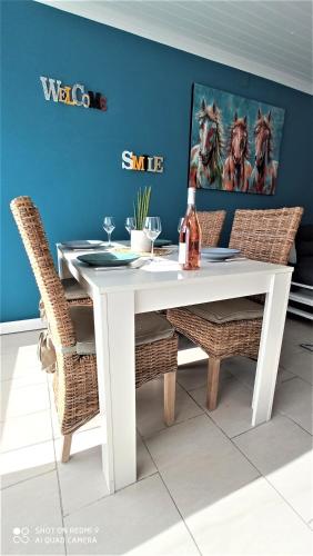a white dining table with wicker chairs and a blue wall at Villa les Palmiers - Aux Portes d'Alès in Saint Julien Les Rosiers