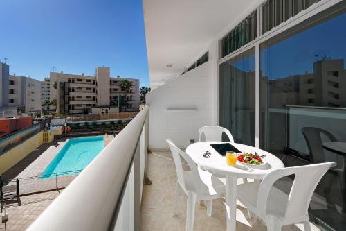 una mesa blanca y sillas en un balcón con piscina en Apartamentos Strelitzias, en Playa del Inglés