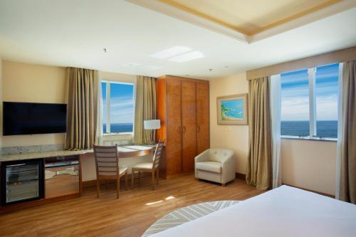 a hotel room with a desk and a table with a room at Windsor Barra Hotel in Rio de Janeiro