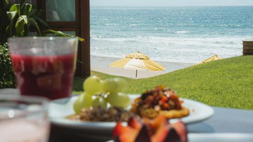 a plate of food and a drink on a table with the beach at Kembali Hotel Porto de Galinhas - Adults Only in Porto De Galinhas