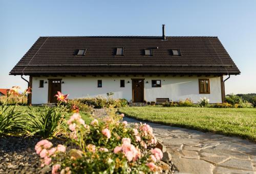 a white house with a black roof and some flowers at Penzion V Poli in Klimkovice
