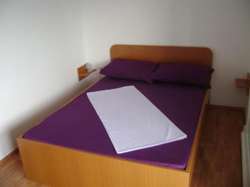 a wooden bed with purple sheets and purple pillows at Guesthouse Lopar (568) in Lopar