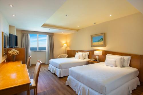 a hotel room with two beds and a table and a desk at Windsor Barra Hotel in Rio de Janeiro