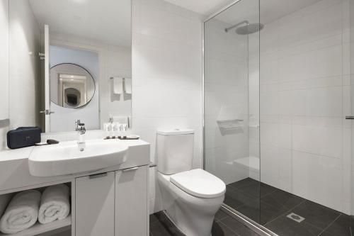 a white bathroom with a toilet and a sink at Quest St Kilda Road in Melbourne