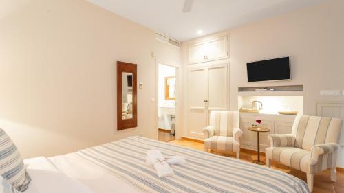 a white bedroom with a bed and two chairs at Real Agua Amarga La Joya - Adults Only in Agua Amarga