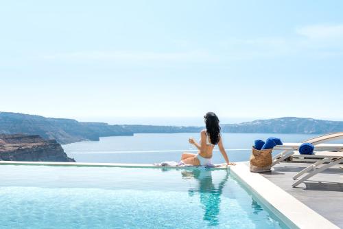a woman is sitting on a balcony overlooking the ocean at Mythical Blue Luxury Suites in Fira