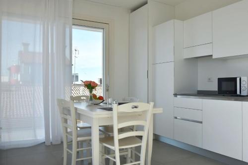 a white kitchen with a table and chairs and a microwave at Residence Al Molo - Agenzia Cocal in Caorle
