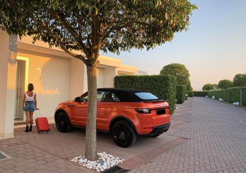 an orange car parked next to a tree with a woman with a suitcase at Pineta Hotel in Monsano