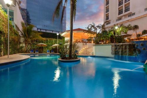 a large blue swimming pool with palm trees and a building at Ramada Plaza by Wyndham Veracruz Boca del Rio in Veracruz